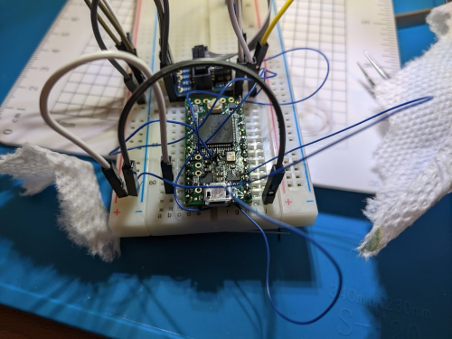 a bunch of wires soldered to a small green board placen on a breadboard, surrounded by jumper wires